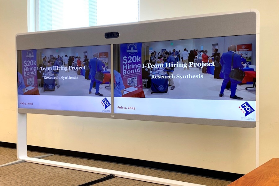 Two large monitors displaying presentation on research findings